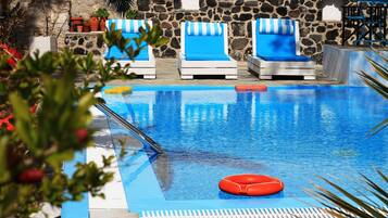 Una piscina con sillones de baño a rayas azules y blancas, un muro de piedra y plantas en macetas.