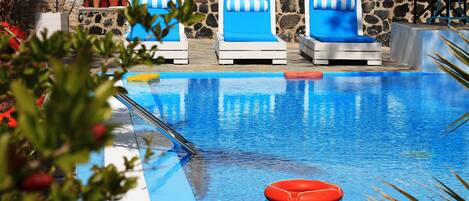 A swimming pool with blue and white striped lounge chairs, a stone wall, and potted plants.