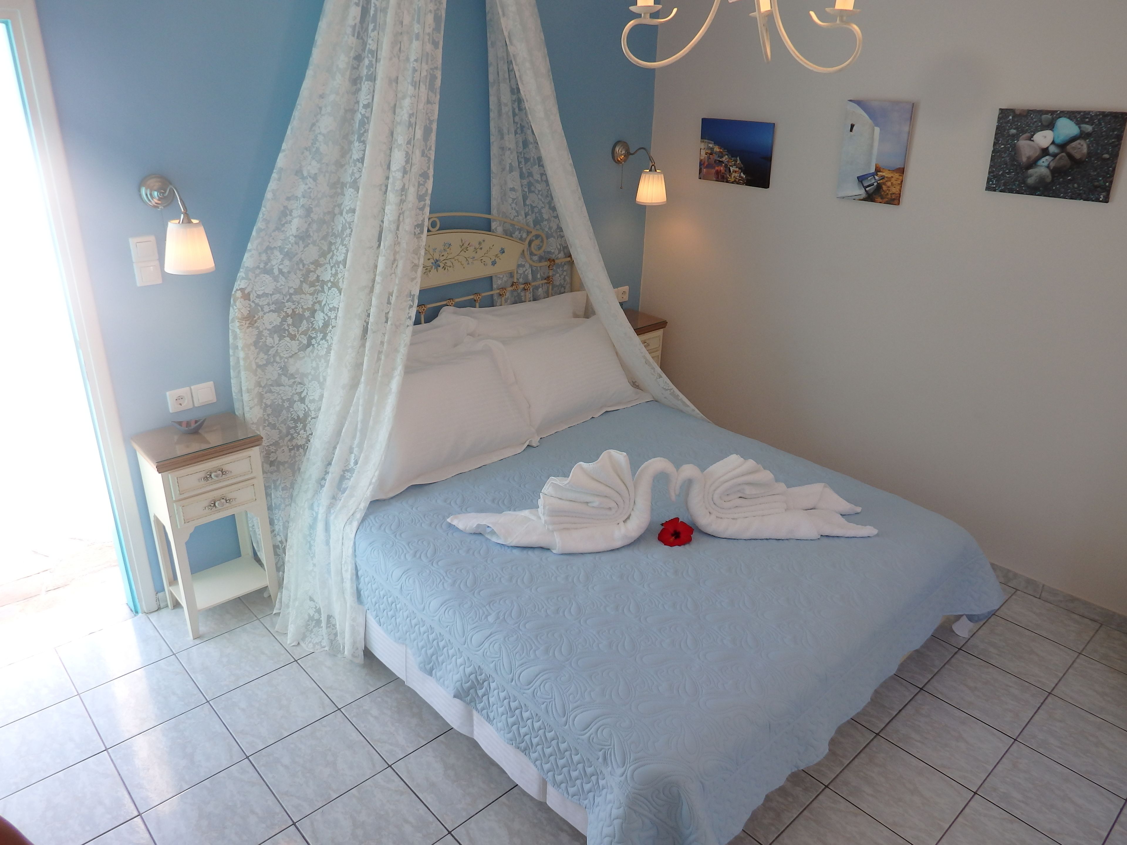A neatly made bed with a blue bedspread and white pillows, a bedside table with a lamp, and a wall with framed pictures.