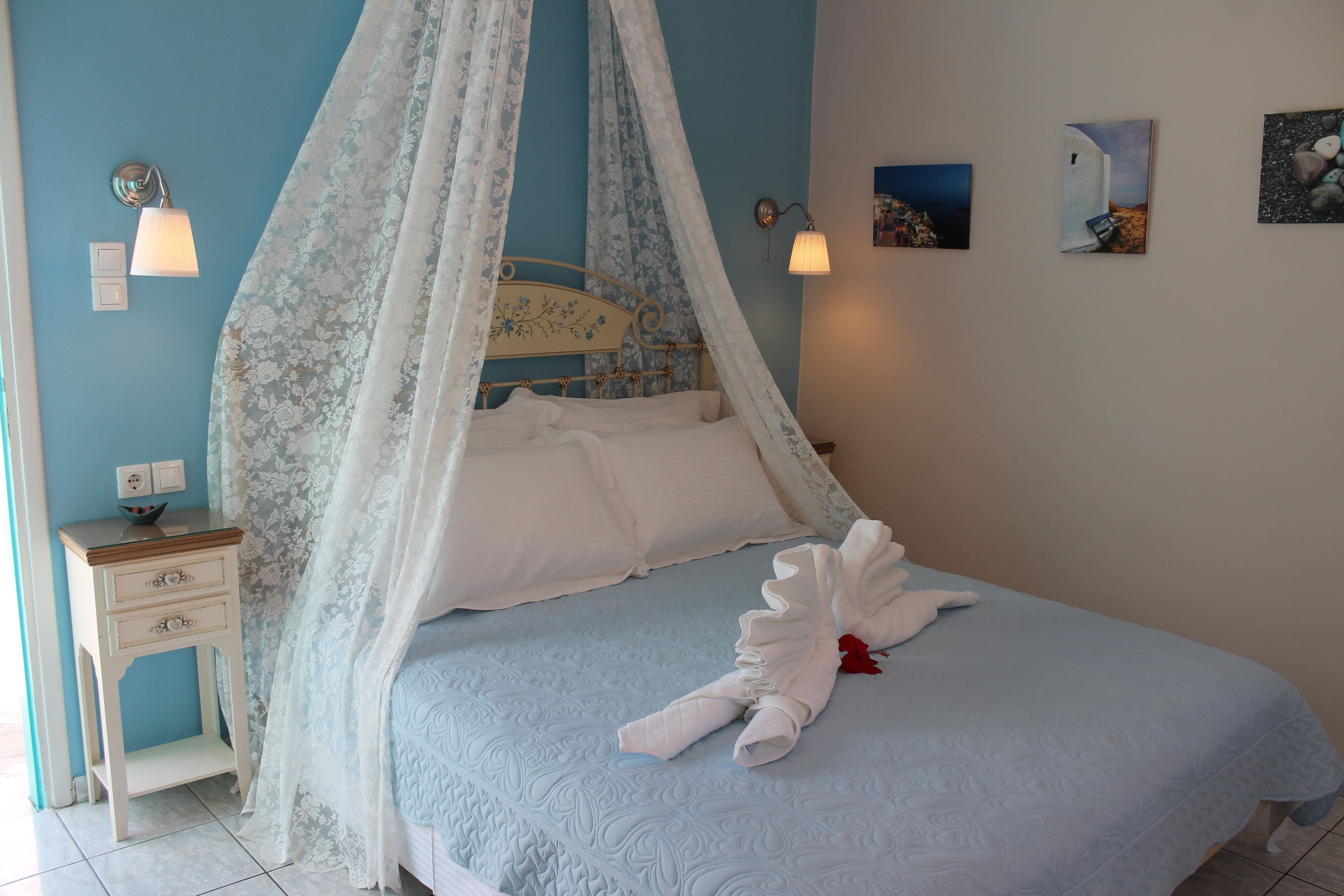 A bedroom with a canopy bed, bedside table, wall-mounted lamp, and artwork.