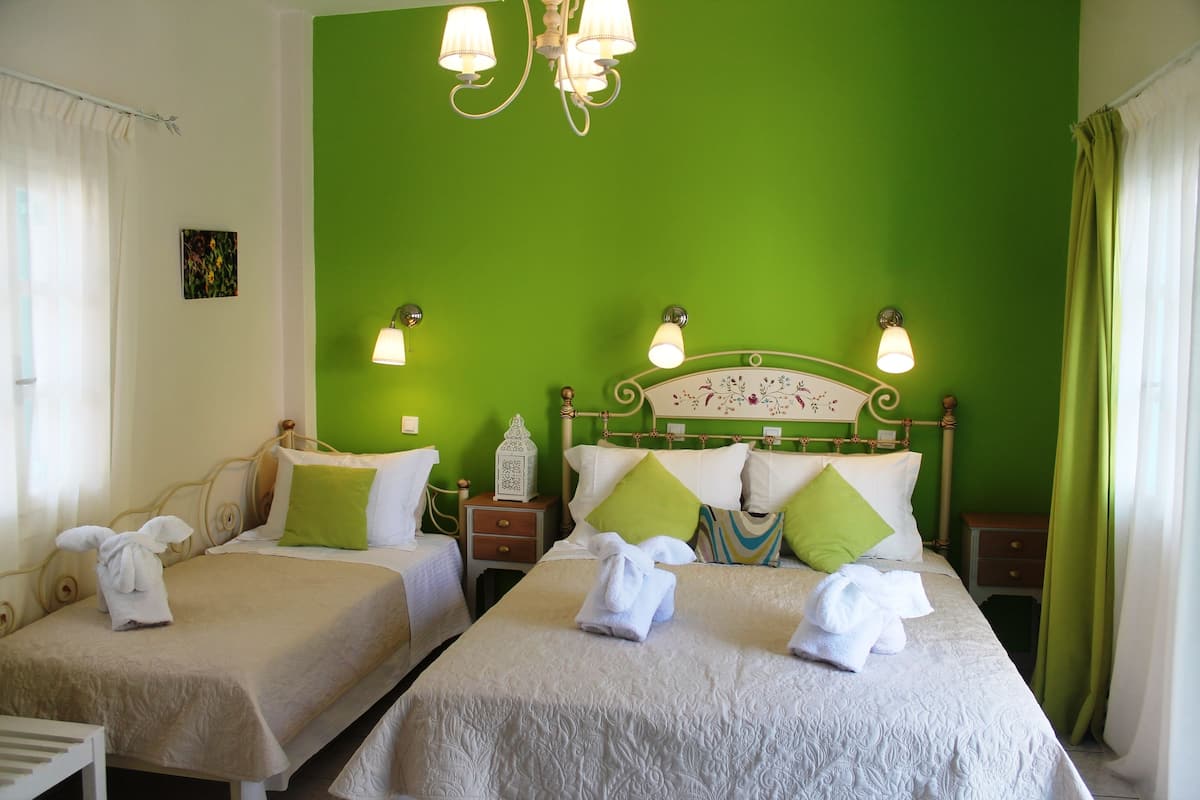 Quarto de hotel com duas camas de solteiro, cada uma com colcha branca e almofadas verdes. Há mesas de cabeceira com luminárias, um candelabro e um pequeno objeto decorativo em uma das mesas.