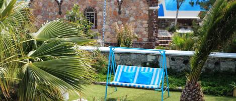A garden with a swing set, palm trees, and a stone building with arched windows.