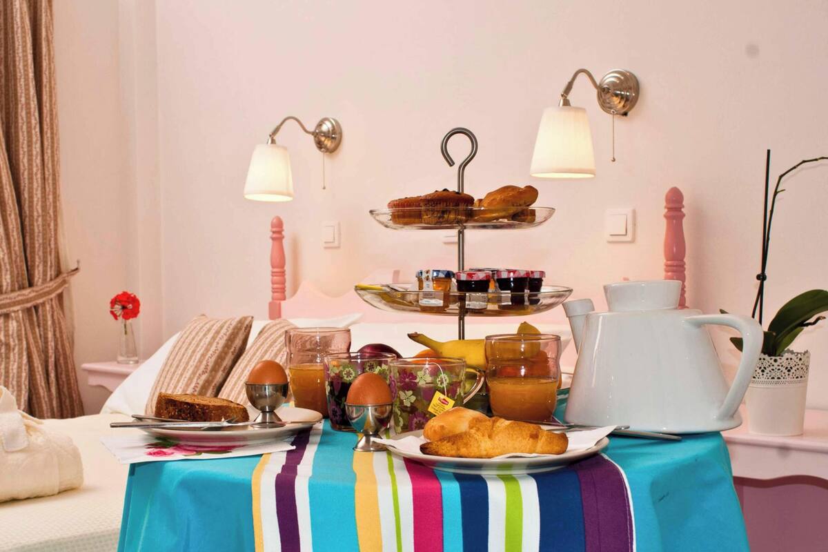 Disposição para café da manhã com um suporte escalonado de doces, uma cafeteira e uma mesa com toalha listrada.