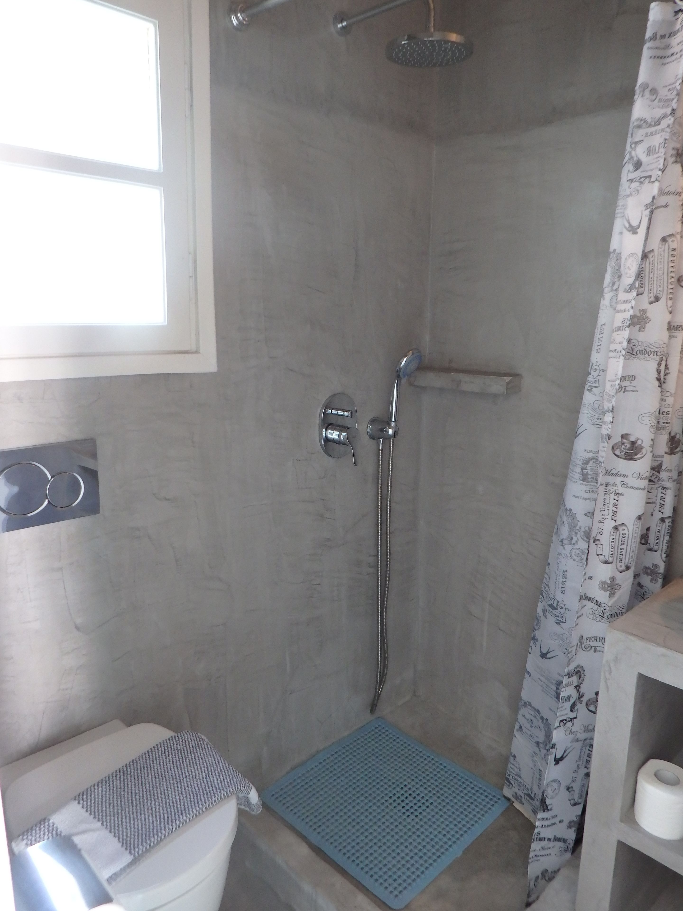 Un espace douche équipé d’un pommeau de douche fixe, d’un pommeau de douche amovible et d’un rideau de douche à motifs.