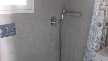 Un espace douche équipé d’un pommeau de douche fixe, d’un pommeau de douche amovible et d’un rideau de douche à motifs.
