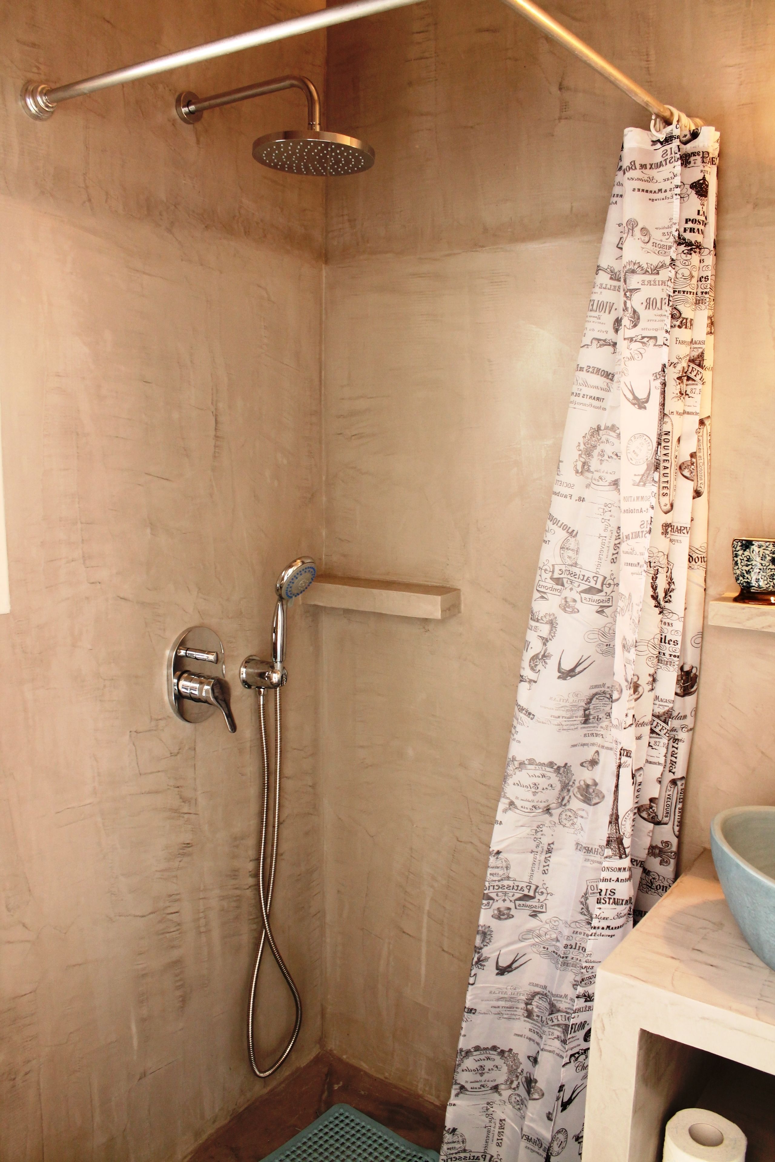 A shower area with a showerhead, handheld shower, and a curtain with printed designs.