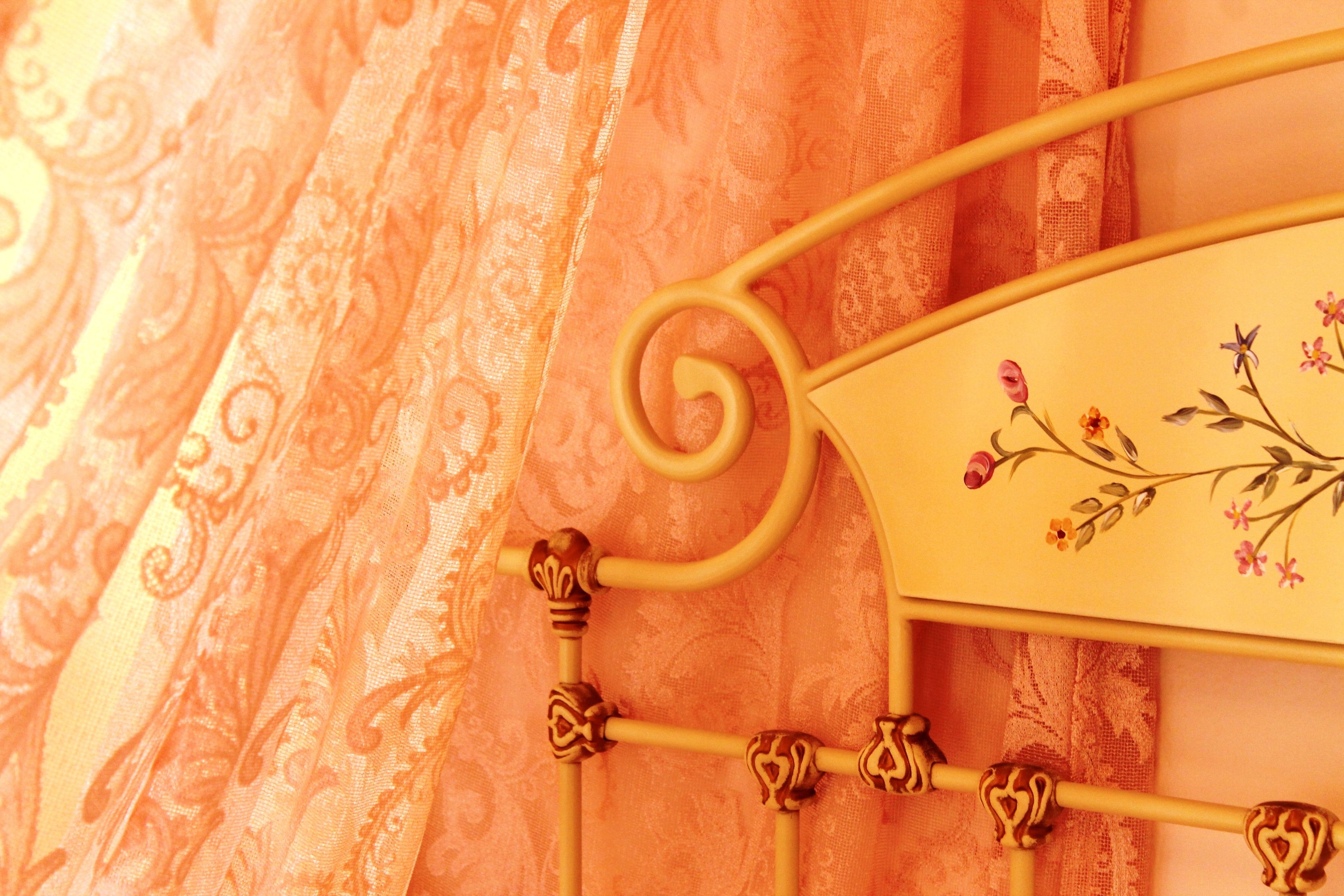 A metal bed frame with ornate floral designs and a curtain with a paisley pattern.