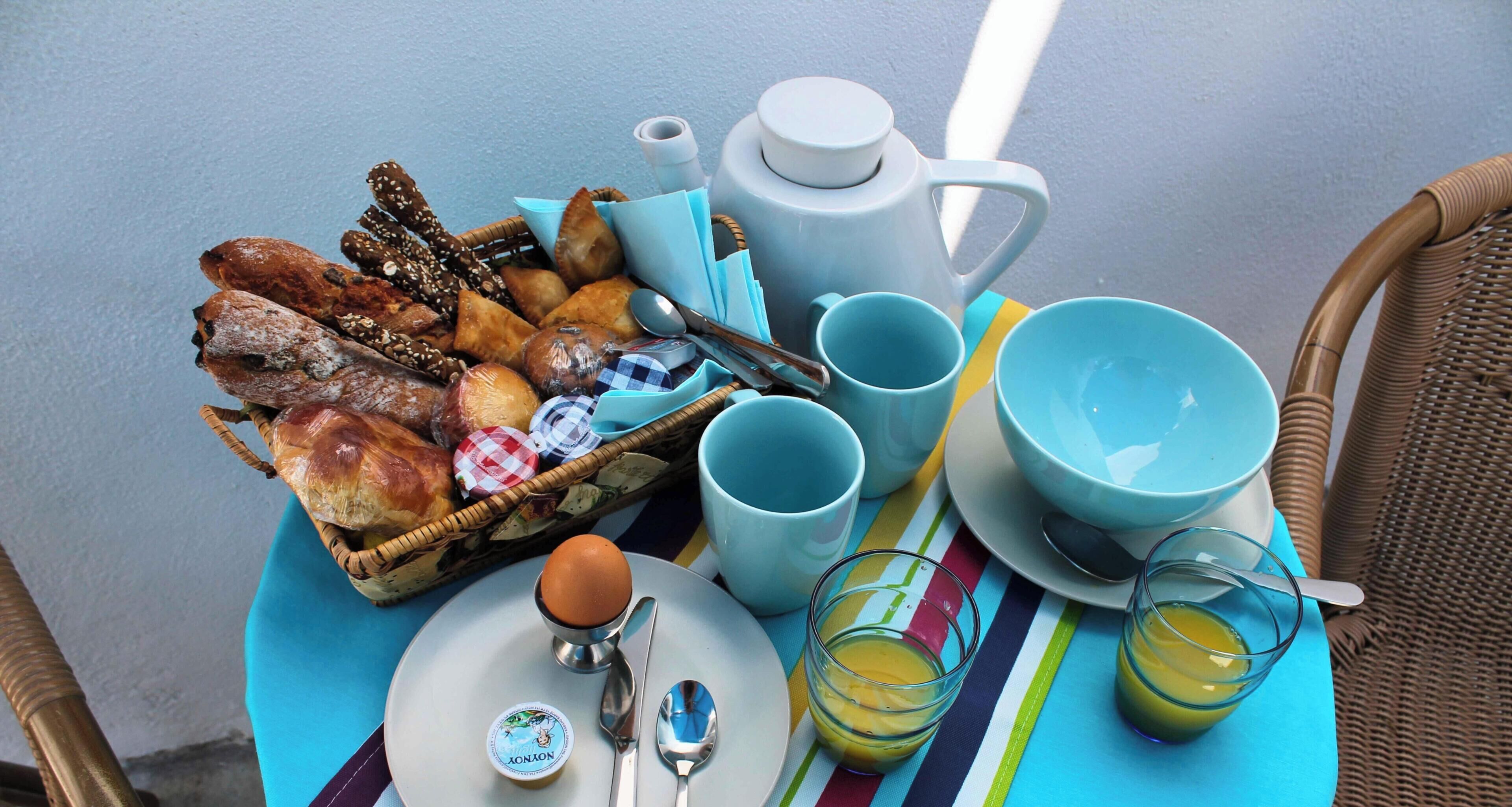 A breakfast tray with pastries, a teapot, cups, and a plate with a boiled egg and a spoon.