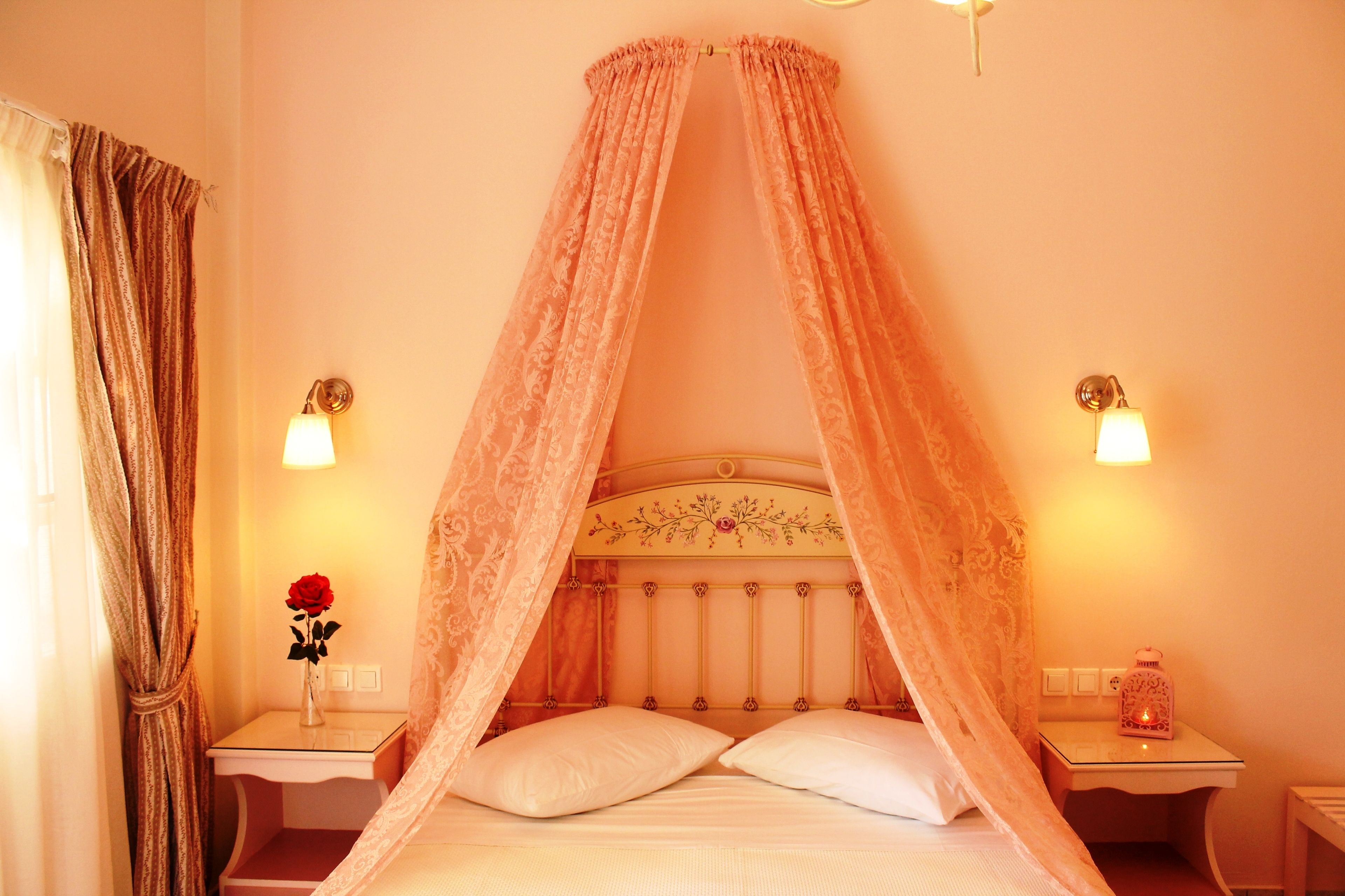 A bed with a canopy, two bedside tables, a vase with a red flower, and wall-mounted lamps.