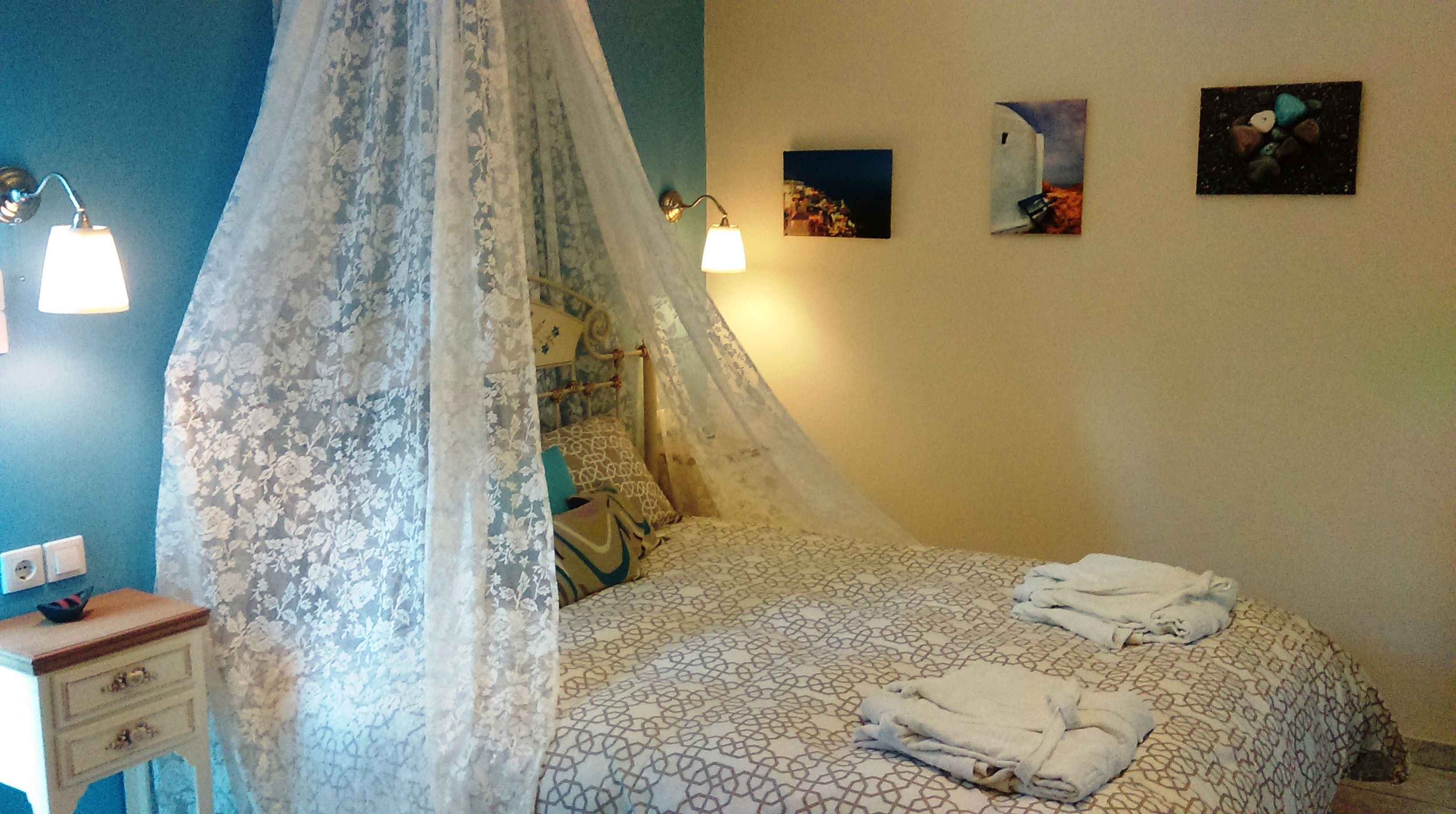 A bedroom with a canopy bed, bedside lamps, a bedside table, and artwork on the wall.