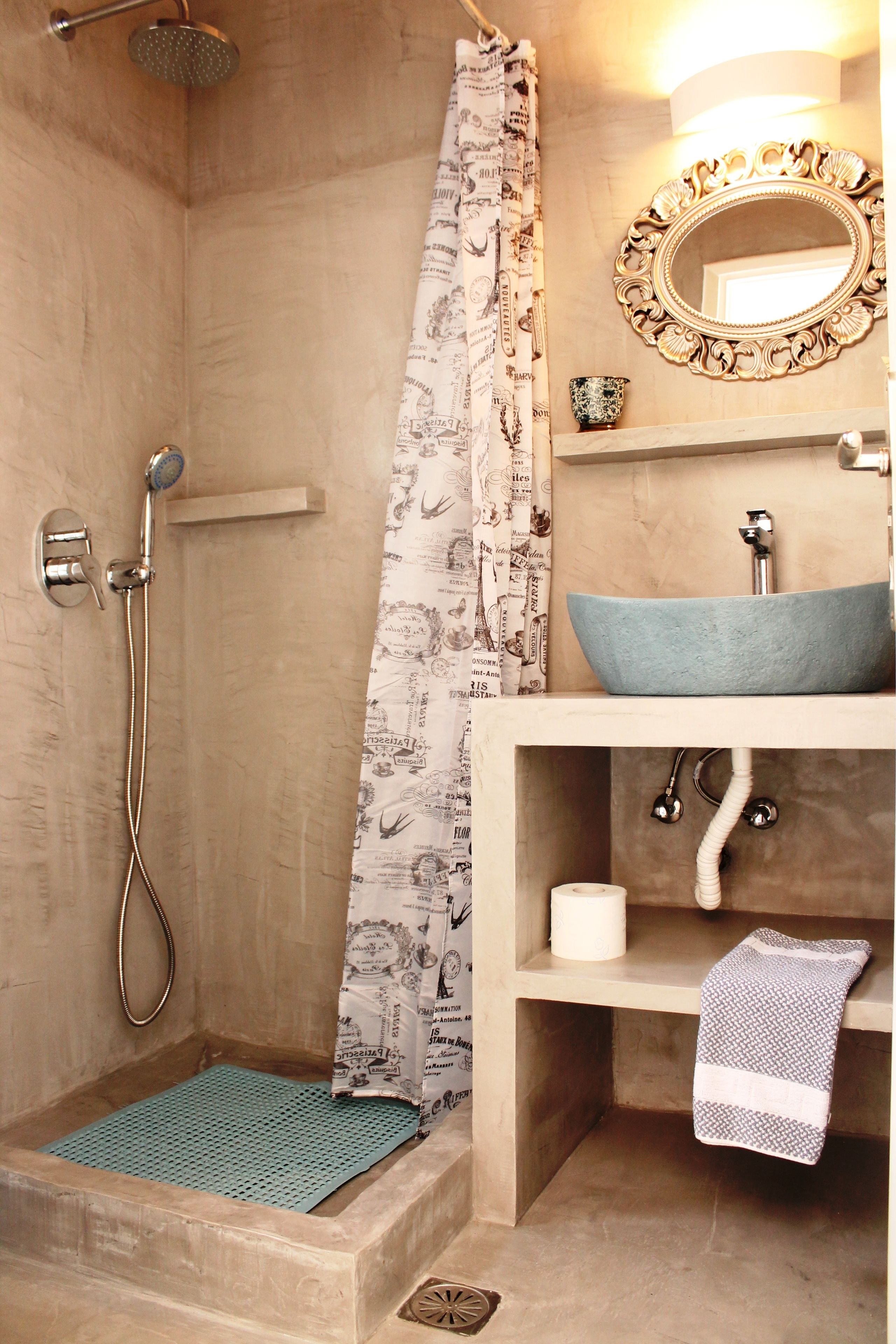 Een badkamer met een douche, een wastafel met een bijzondere wasbak, een spiegel met een sierlijke lijst en een handdoek aan de muur.