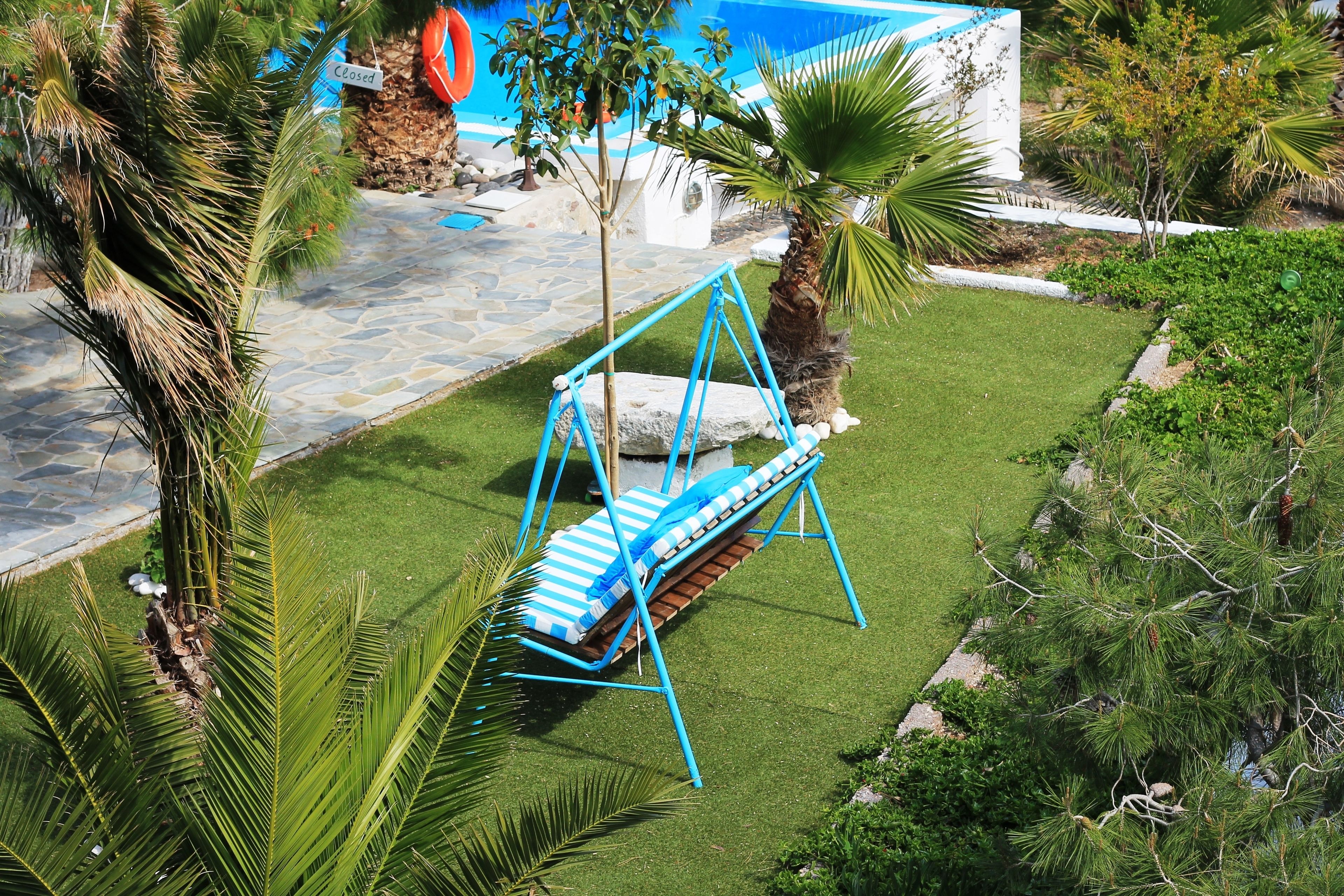 A blue swing chair with a striped cushion in a well-maintained garden with palm trees and a stone pathway.