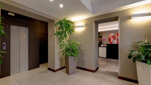 A modern hotel lobby with a reception desk, a large potted plant, and an elevator. - Hotel Rinascimento  (Rome)