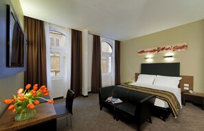 A hotel room with a bed, a desk with a vase of flowers, a chair, a sofa, and a painting on the wall. - Hotel Rinascimento  (Rome)