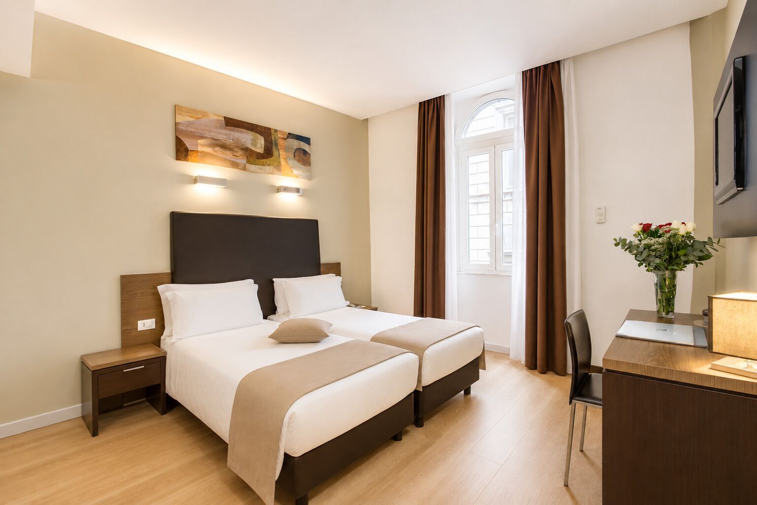 Une chambre d’hôtel comprenant un lit, des tables de chevet, un bureau avec une lampe, un téléviseur à écran plat et une fenêtre avec des rideaux.