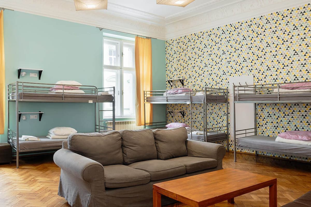 A dormitory room with bunk beds, a sofa, a wooden table, and a patterned wall.