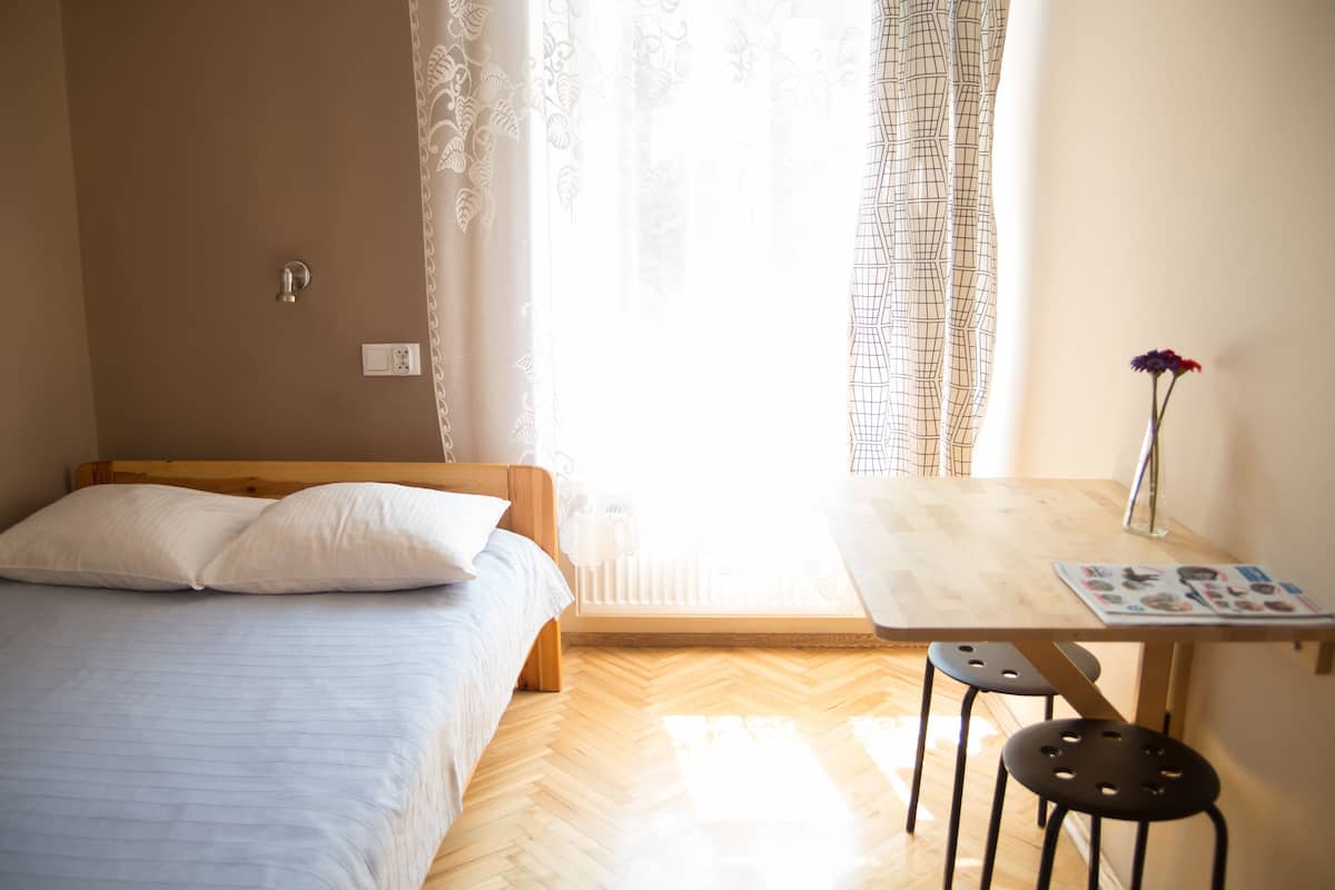 A bedroom with a bed, a small table with a vase, and a window with curtains.