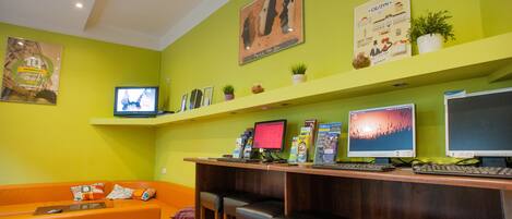 A reception area with a wooden desk, two computer monitors, a television, and a green wall with artwork.