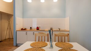 A modern kitchen with white cabinets, a wooden countertop, and a dining table with woven placemats. - Dizzy Daisy Hostel (Kraków)