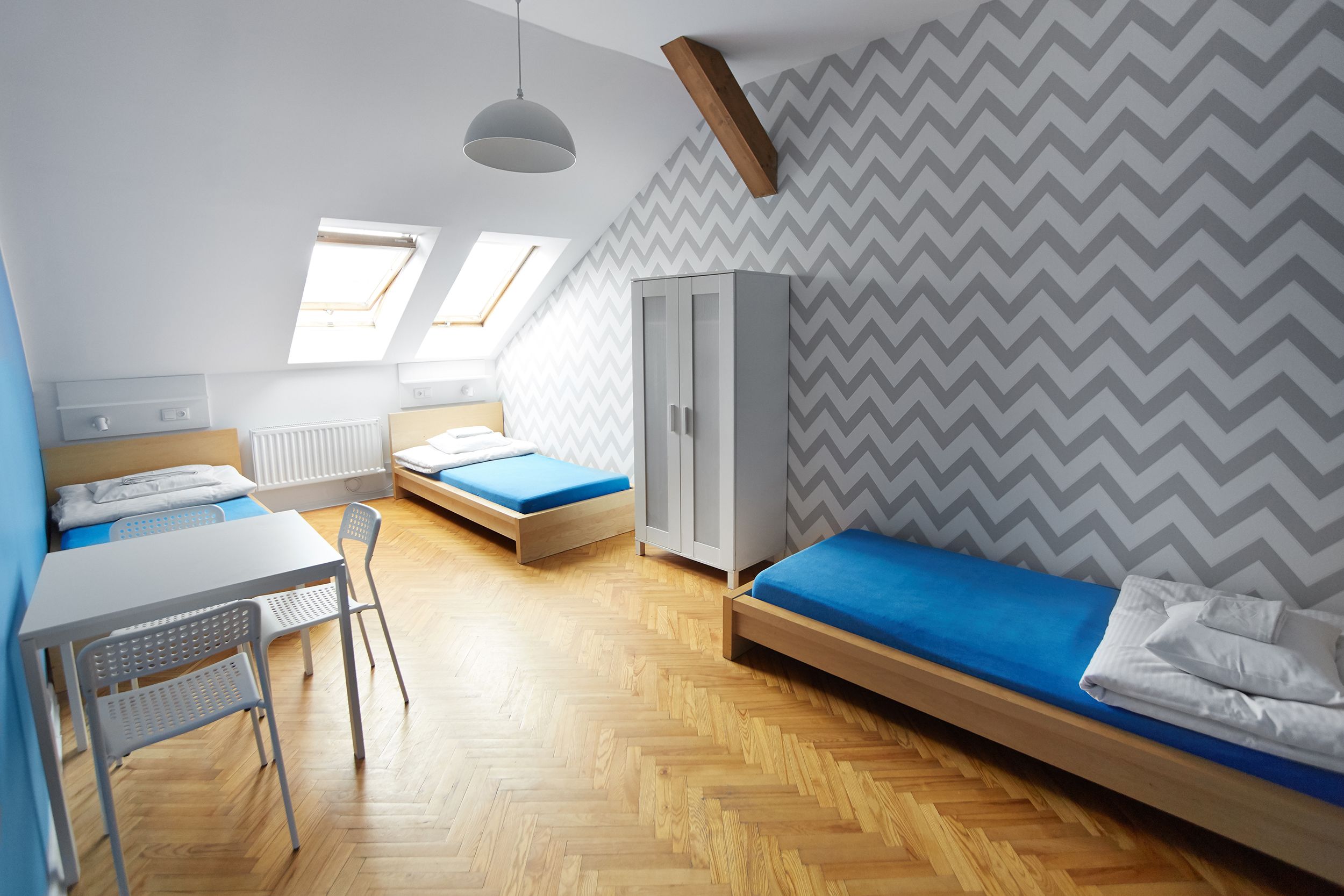 Habitación tipo dormitorio con dos camas, un escritorio, una silla, un armario y tragaluces.