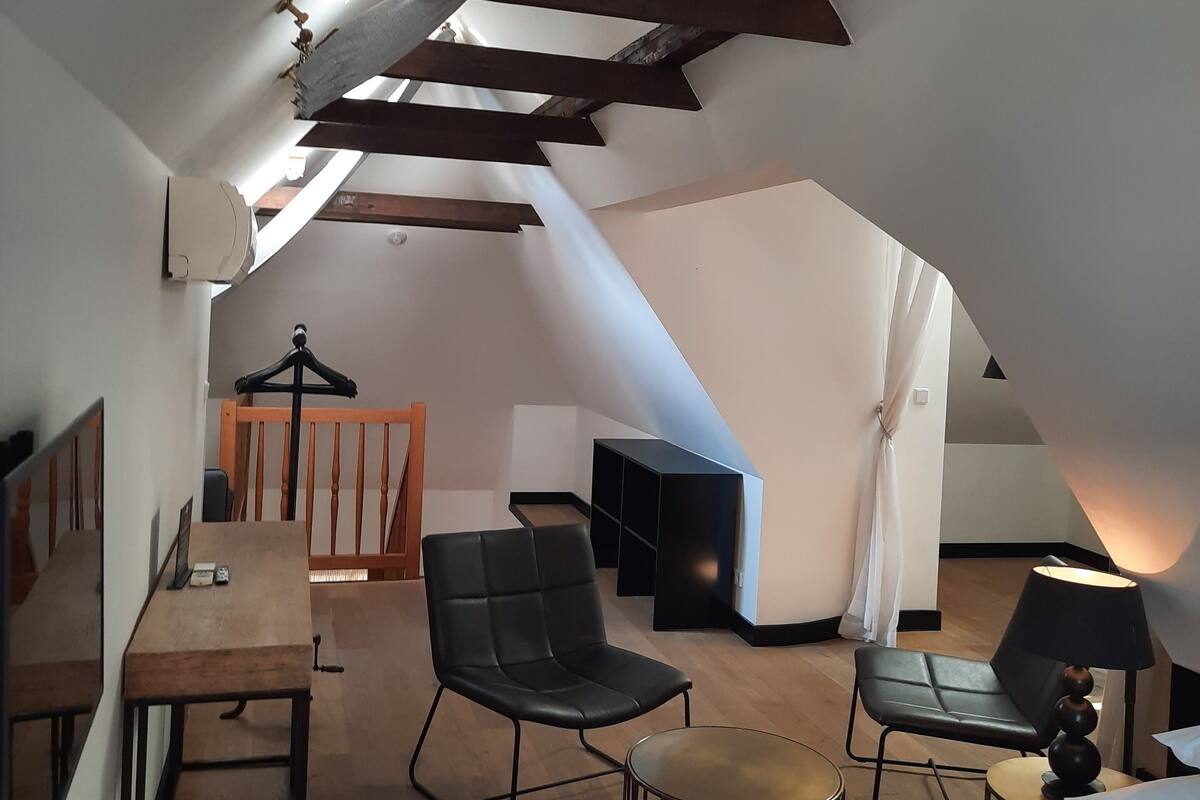 A modern, compact room with a sloped ceiling, a bed, a desk, a chair, and a small table.