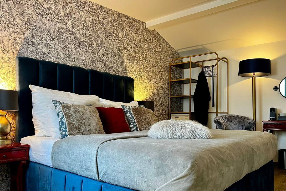 A bedroom with a large bed, a nightstand, a lamp, a wardrobe, and a mirror.