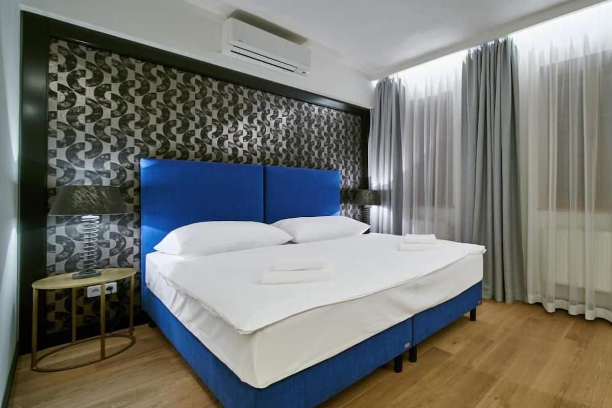 A neatly made bed with white linens, a blue headboard, and a patterned wall.