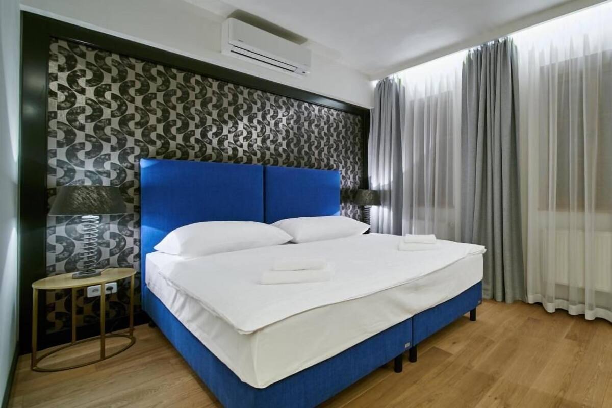 A neatly made bed with white linens, a blue headboard, and a patterned wall.