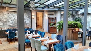 Ravintola, jossa on siniset samettituolit, puupöydät ja lasikatto.