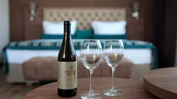 A hotel room with a bed, a wooden table with a bottle of wine and two glasses.