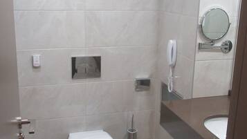 A modern bathroom with a toilet, a hand dryer, a trash can, and a mirror.