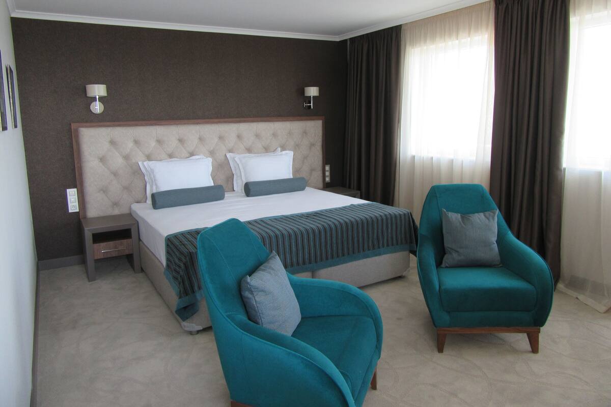 A hotel room with a large bed, two armchairs, a nightstand, and a lamp.
