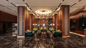 Eine Lobby mit einer Rezeption, grünen Sofas und einer Kristallleuchtre.