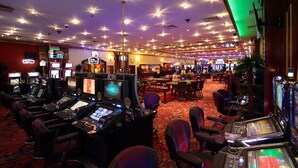 Ein Casino mit mehreren Spieltischen und Spielautomaten, einem Teppichboden und einer Decke mit zahlreichen Lampen.