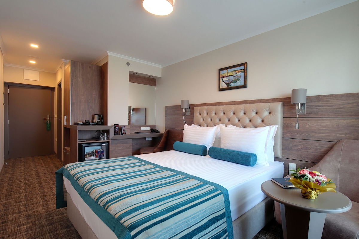 Une chambre d’hôtel avec un grand lit, un petit bureau, une chaise, une table de chevet avec une lampe et un téléviseur fixé au mur.