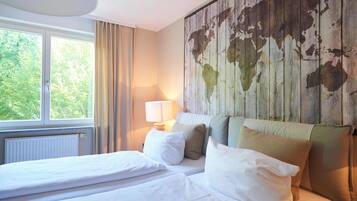 A hotel room with a bed, a window with curtains, a lamp, and a world map on the wall.