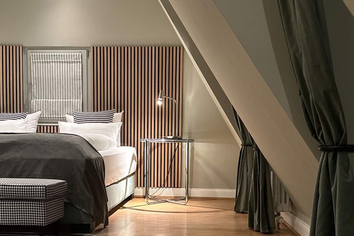 A modern bedroom with a large bed, a bedside table, a floor lamp, and a window with blinds.