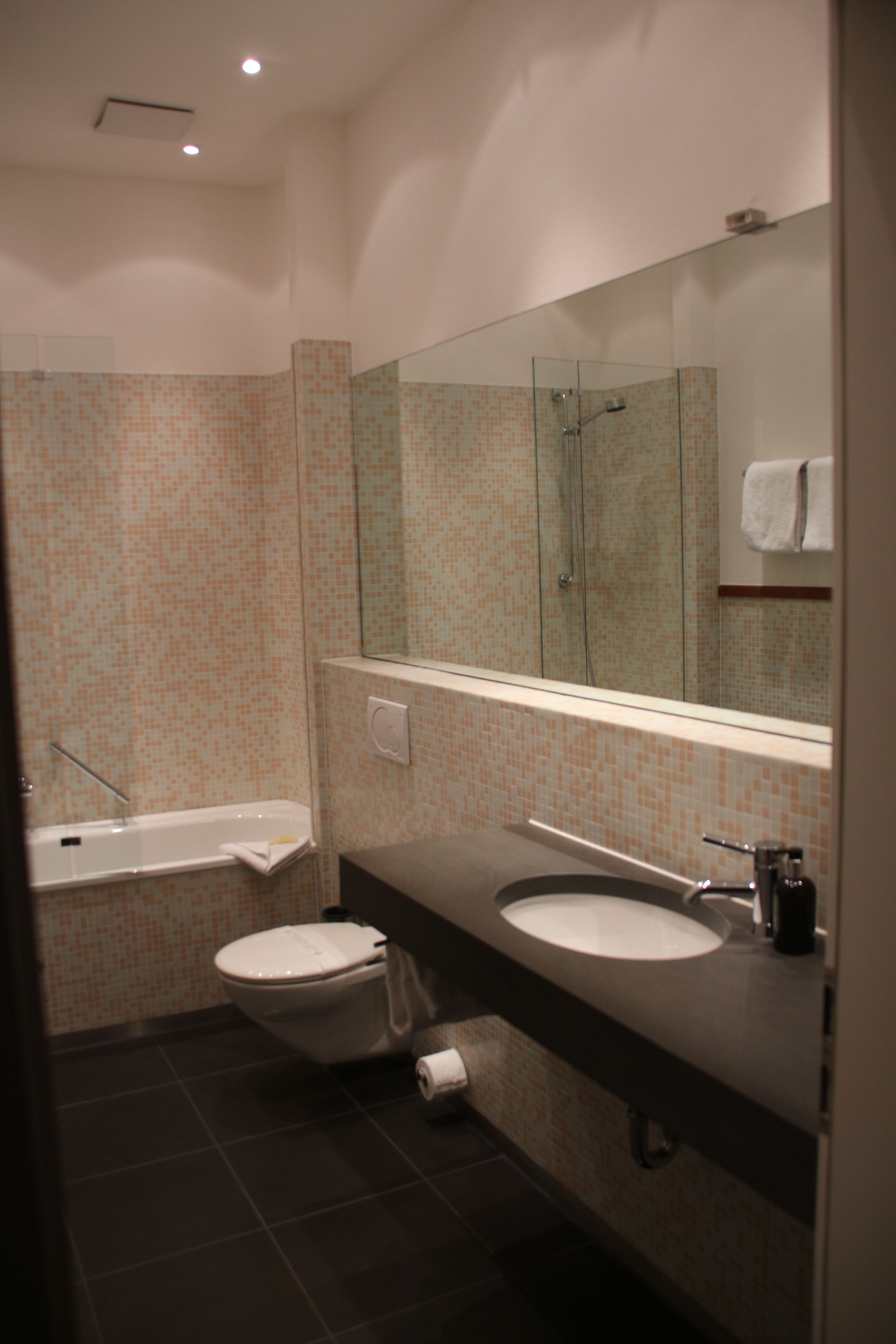 Een moderne badkamer met een badkuip, twee wastafels, een toilet en een grote spiegel.