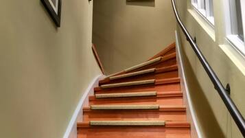 A wooden staircase with handrails, framed pictures on the walls, and a window with blinds.