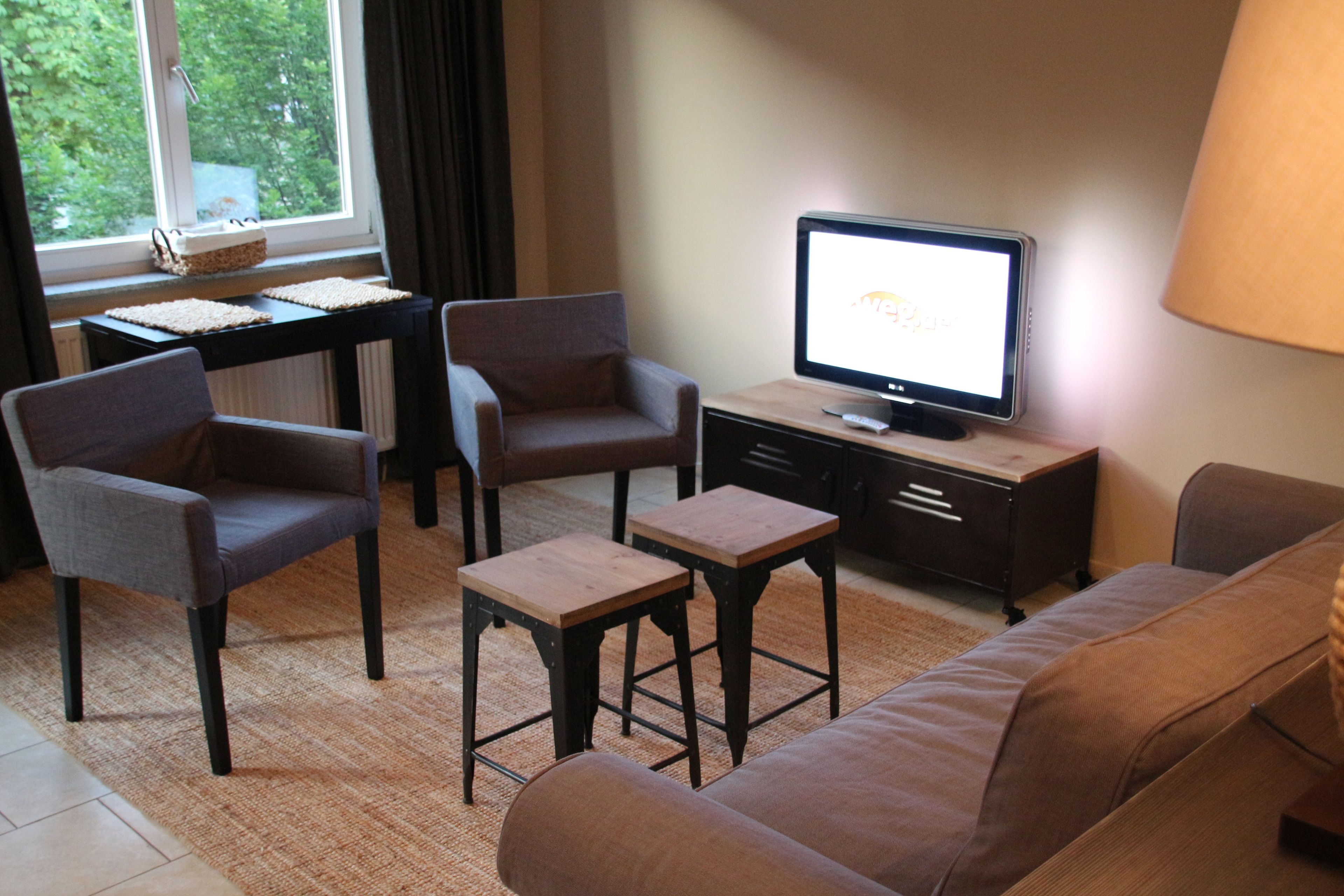 Una sala de estar con un sofá, dos sillones, una mesa de centro, un televisor y una lámpara.
