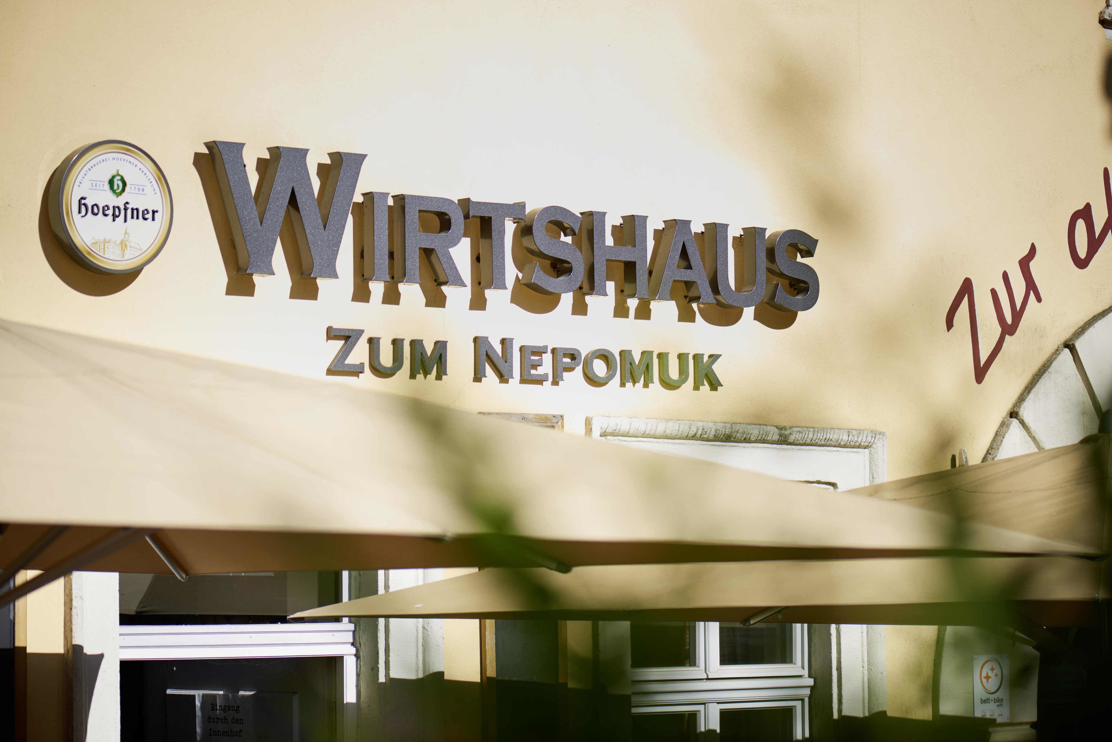 Een bord met 'WIRTSHAUS ZUM NEPOMUK', een logo en tekst.