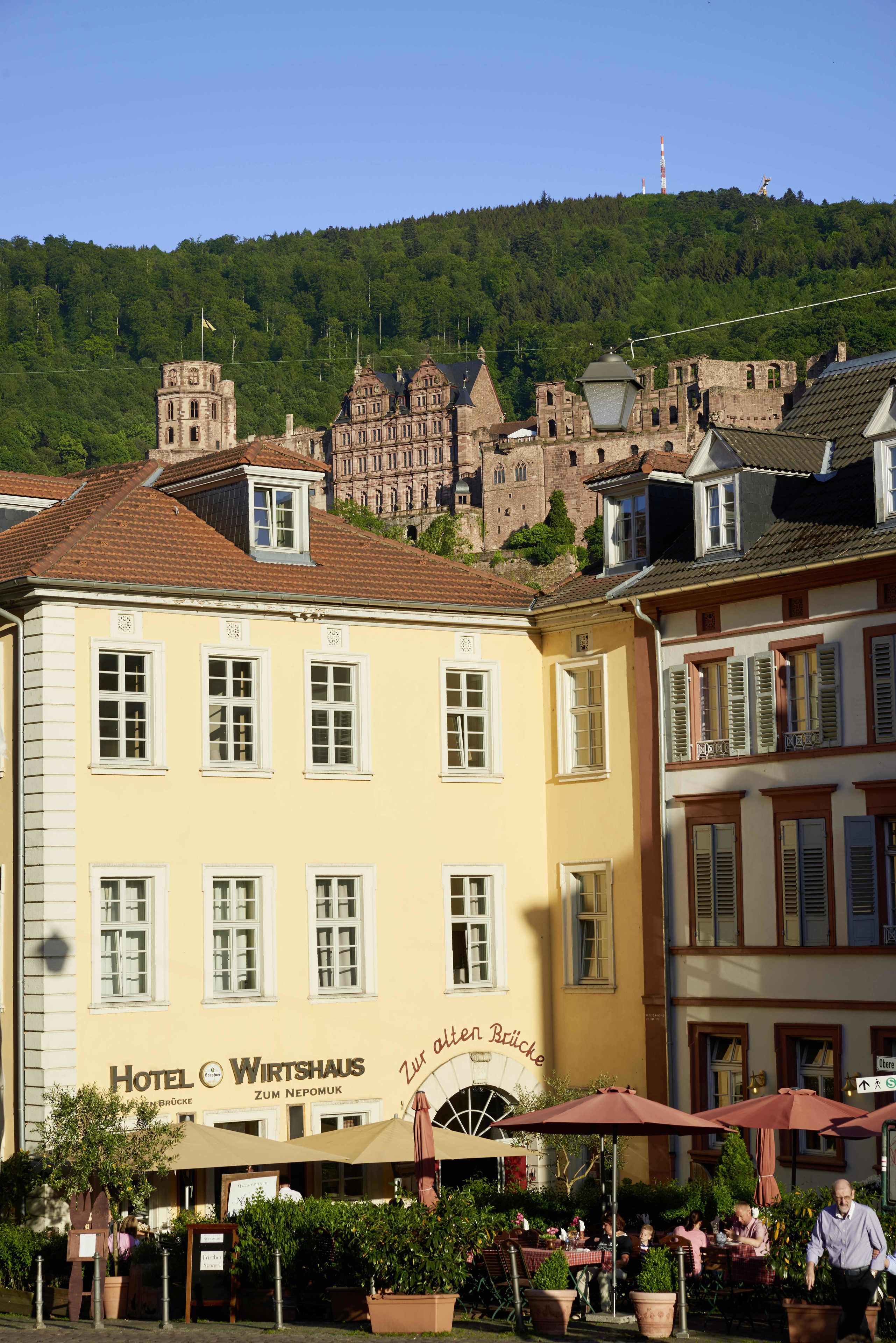 Un hotel con un letrero que dice "Hotel Wirtshaus Zum Nepomuk" y mesas al aire libre con sombrillas.