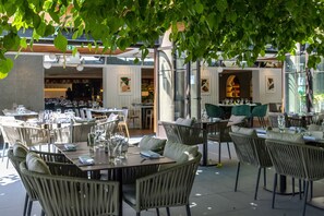 Un espace extérieur aménagé pour les repas, avec des tables et des chaises, une entrée avec une porte vitrée et une vue sur l’intérieur.