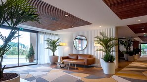 A modern lobby with a wooden ceiling, a large potted plant, a sofa, and a large mirror. - Servotel Saint-Vincent (Nice)