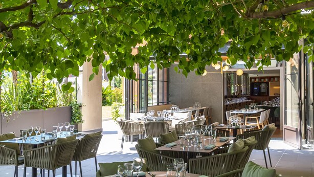 An outdoor dining area with round tables and wicker chairs, surrounded by lush greenery. - Servotel Saint-Vincent (Nice)