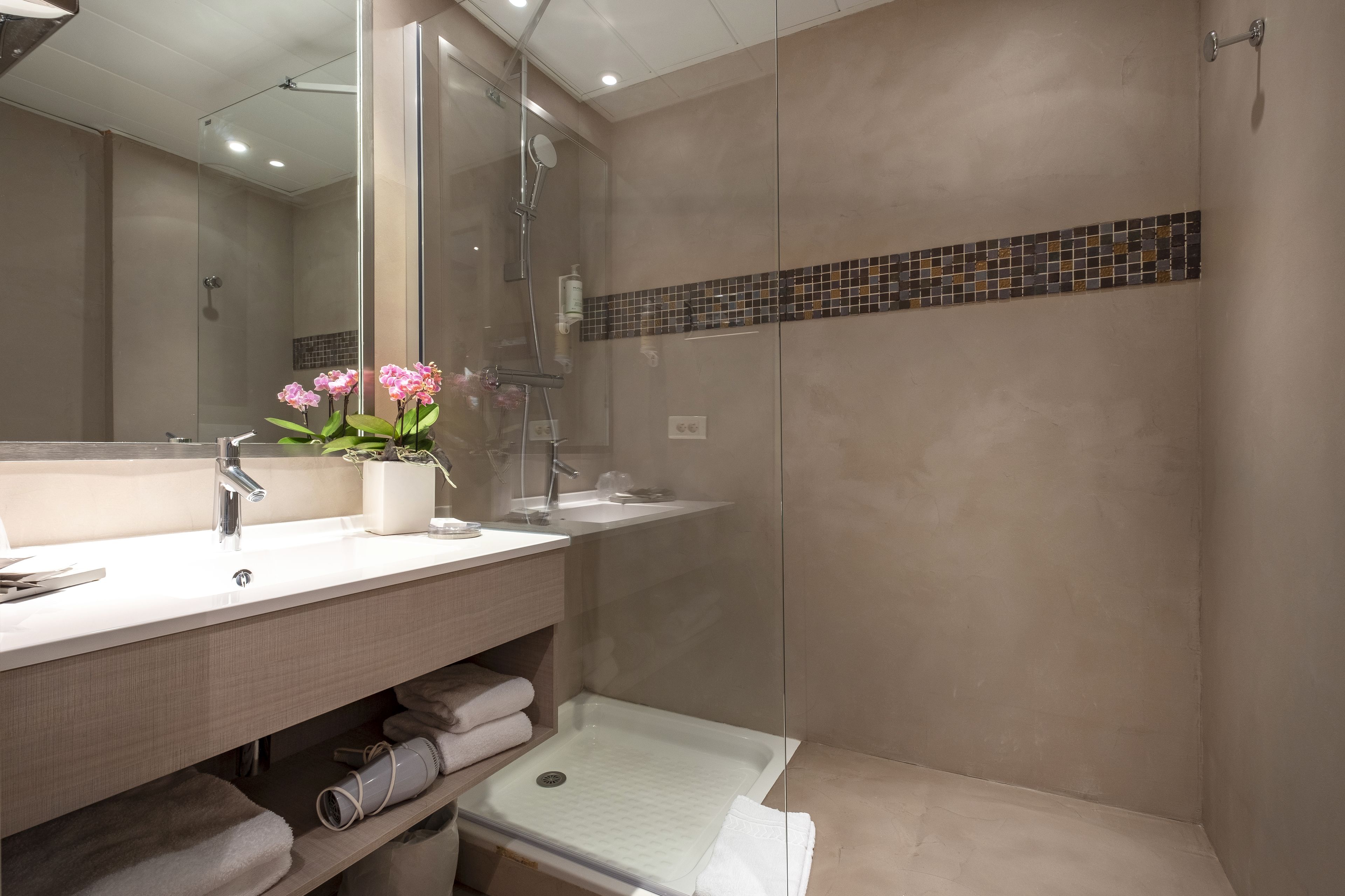 A modern bathroom with a large mirror, two sinks, a shower, and a tiled backsplash.