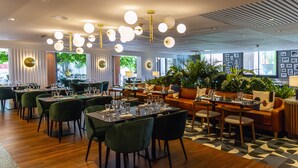 A modern restaurant with round tables, green chairs, and a ceiling with hanging lights. - Servotel Saint-Vincent (Nice)