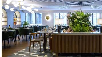 A modern restaurant with a central island, round tables, and green chairs.