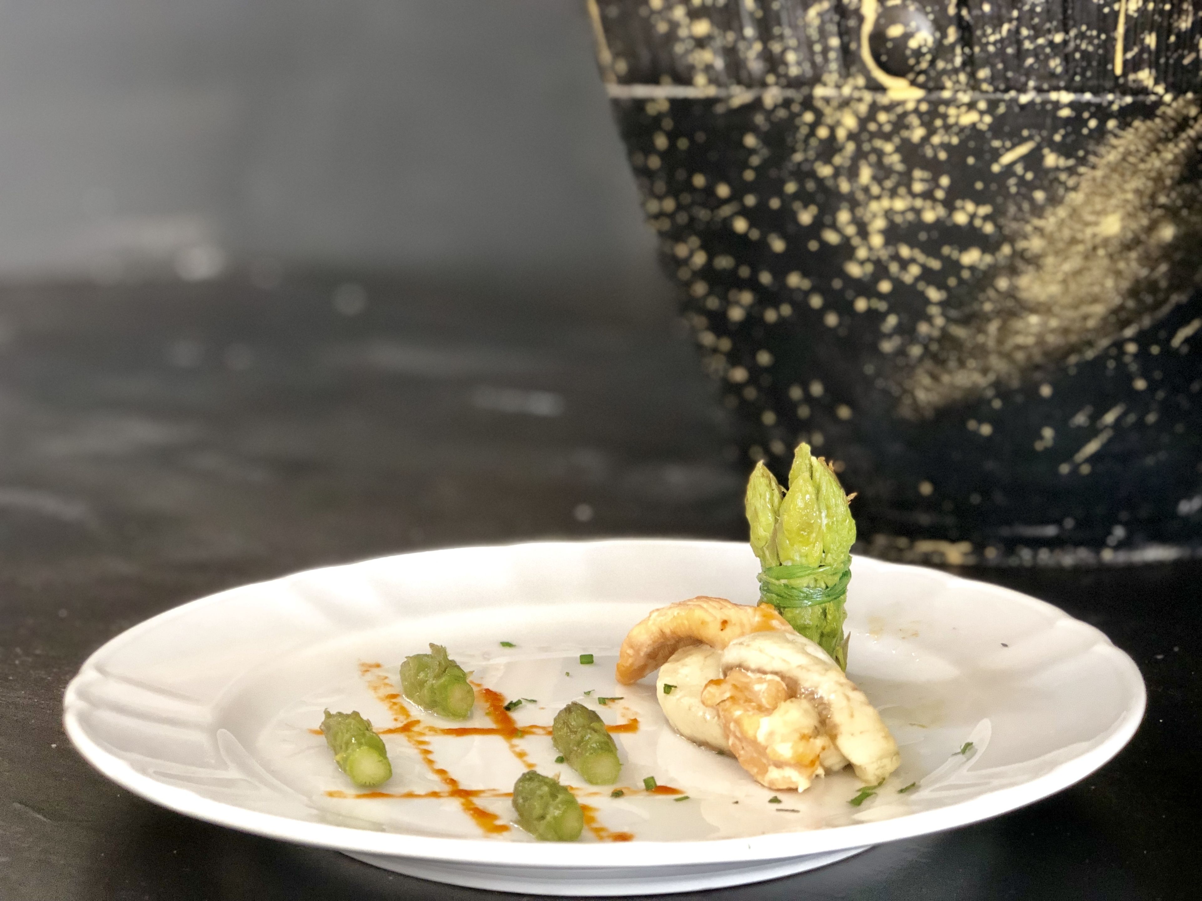 Un piatto con cibo, una foglia decorativa e un vaso nero con riflessi dorati.