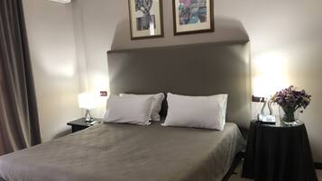 Une chambre d’hôtel avec un lit, deux oreillers blancs, une table de chevet avec une lampe, un vase de fleurs et deux œuvres d’art encadrées accrochées au mur.